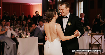 A newly wed couple dance in a dark room while the guests look on with affection.