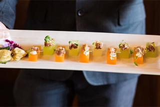 A serving dish with appetizers held by a person wearing a grey suit