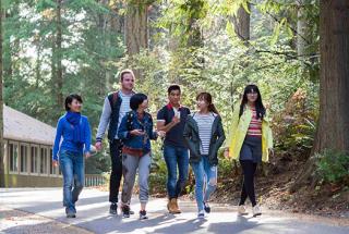 A group of six Royal Roads students walk along a wooded trail in conversation